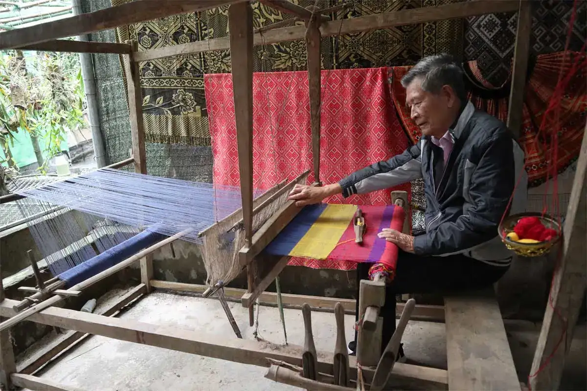 Thai woman weaving colorful traditional brocade on a wooden loom in Pom Coong Village, Mai Chau