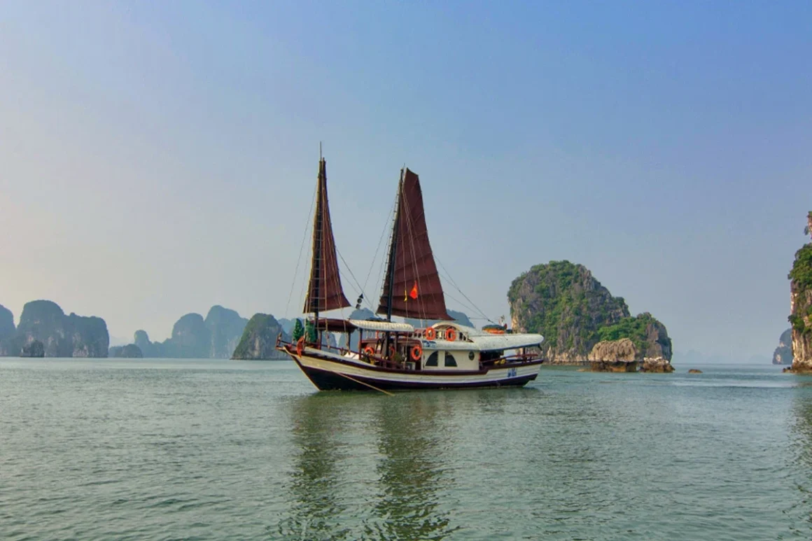 Traditional wooden L'Amour Junk sailing on the turquoise waters of Bai Tu Long Bay